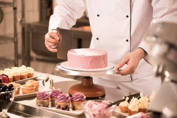 Obraz na płótnie Canvas cropped shot of confectioner making cake in restaurant kitchen