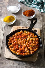 Fried spicy chickpeas in frying pan on wooden table