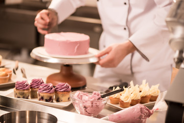 cropped shot of confectioner making cake in restaurant kitchen