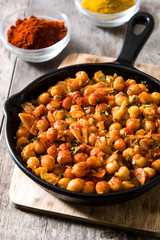 Fried spicy chickpeas in frying pan on wooden table