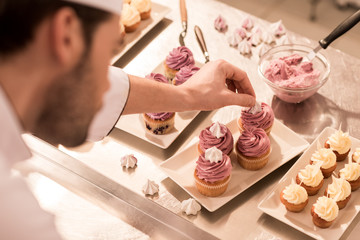 selective focus of confectioner decorating cupcakes in restaurant kitchen