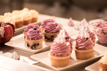 close up view of sweet cupcakes on plates on counter in restaurant kitchen