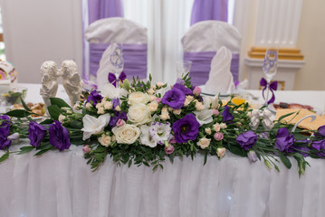 Beautiful purple and creamy flowers on table of newlyweds at wedding reception in restaurant, free space. Wedding table decorated with flowers, served for two people. Wedding table decoration newlywed