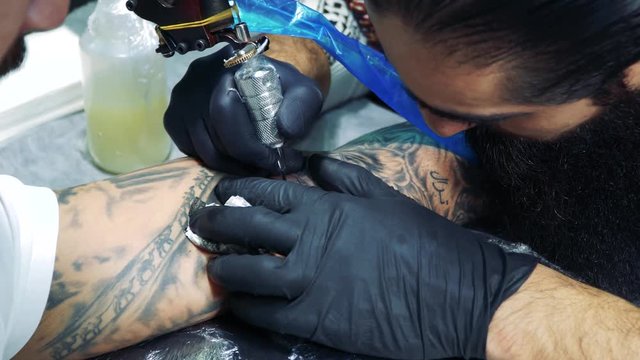 Master makes tattoo pictures in tattoo studio./Professional tattooist at work in tattoo parlor.