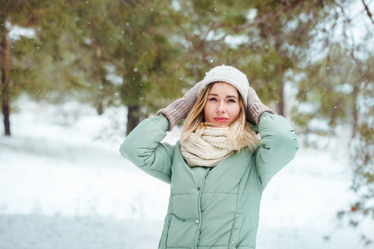 Young beautiful slender blonde girl smiles and looks at the camera outdoors in winter. Portrait of an attractive model on a winter background. Space for text.