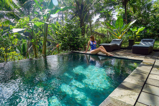 A young girl sits on the edge of an infinity pool in the jungle. Taken on the island of Bali in Ubud.