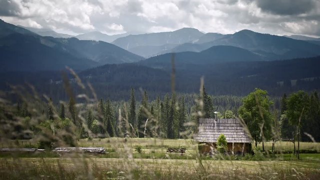Timelaps of mountains with the hut. Grass fluttering in the wind in the foreground. 4k HDR H264