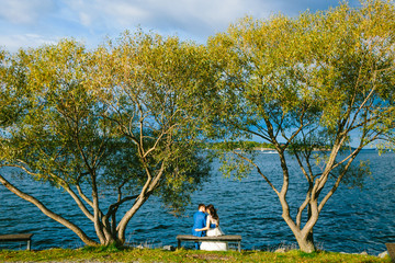 Newlyweds are relaxing on a bench and sitting before a river. Bride and groom is resting on nature