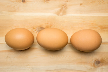 Three chicken eggs lie on a wooden board