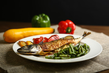 Healthy and proper food, grilled fish and vegetables with lemon and green beans on a white plate. On the background of pepper, burlap and wooden table. Low-calorie food