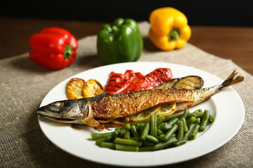 Healthy and proper food, grilled fish and vegetables with lemon and green beans on a white plate. On the background of pepper, burlap and wooden table. Low-calorie food