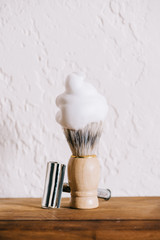 close up view of shaving brush with foam and blade against white wall