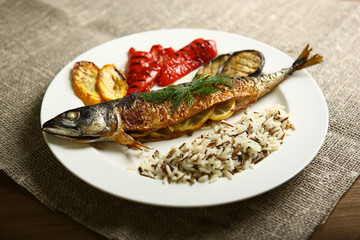 Healthy and proper food, grilled fish and vegetables with lemon and black and white rice on a white plate. Against the background of sacking and a wooden table. Low-calorie food