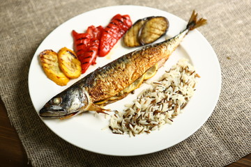 Healthy and proper food, grilled fish and vegetables with lemon and black and white rice on a white plate. Against the background of sacking and a wooden table. Low-calorie food