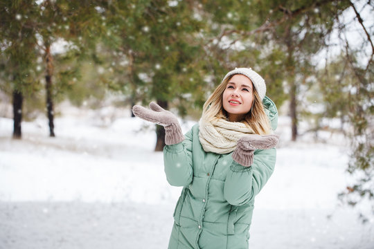 Young beautiful girl looks at falling snow and catches snowflakes. Portrait of an attractive girl on a winter background. Space for text.