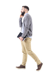 Relaxed successful businessman on the phone walking and carrying tablet computer. Full body length portrait isolated on white studio background. 