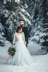 Fototapeta na wymiar Bearded man and his lovely bride pose on the snow in a magic winter forest