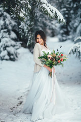 Fototapeta na wymiar Lovely bride poses with rich wedding bouquet in a winter forest