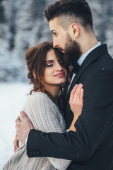 Bearded man and his lovely bride pose on the snow in a magic winter forest