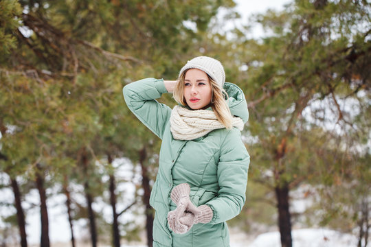 Young beautiful slender blonde girl outdoors in winter looking away. Portrait of an attractive model on a winter background. Space for text.