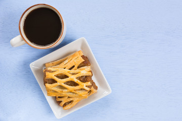 top view of pineapple pie in a ceramic dish and a cup of coffee on light blue wooden background with copy space.