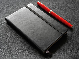 black notebook with red pen on a leather surface