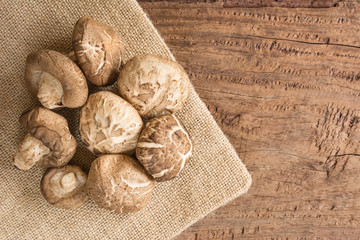 pile of raw shiitake mushroom on sack cloth with old and crack wooden background, top view. alternative healthy food and medical concept.