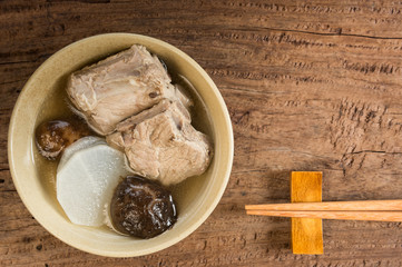pork rib clear soup with white radish and shiitake mushroom in a ceramic bowl on wooden table, top view. healthy food concept.