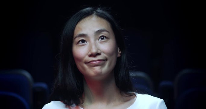 Asian woman at the movie theatre reacts to a heart warming moment in a movie.