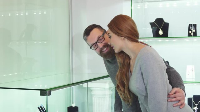 Mature bearded man embracing his beautiful wife while choosing jewelry together at the boutique love relationships people anniversary consumerism shopping buying customers.