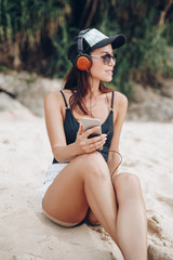 young beautiful woman listening music with headphones at tropical beach