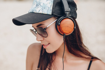 Naklejka premium beautiful young woman in cap and sunglasses listening music with headphones