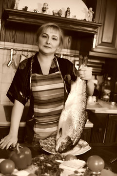 middle-aged woman in the kitchen with a big fish, going to cook