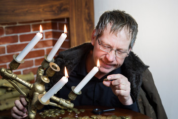 A rich greedy elderly man looks at coins under the light of a burning candle. The collector looks...