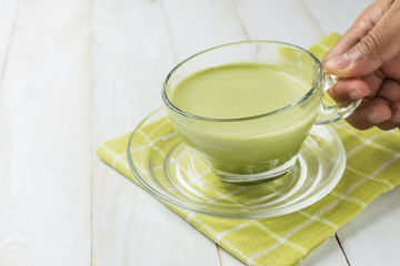 Hand holding green tea glass on white wood background.Green tea is beneficial to the body, antioxidants.