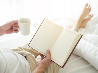 Young asia man drinking coffee on bed while reading a book