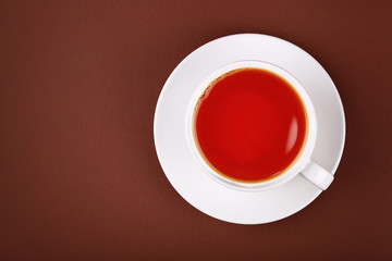 Full white cup of red black tea on brown