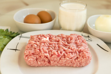 pork minced meat on a plate, ingredients for cooking meat cutlets, 2 eggs, a glass of milk, onion, food