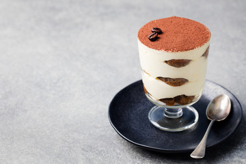 Tiramisu, traditional Italian dessert in glass on a grey stone background