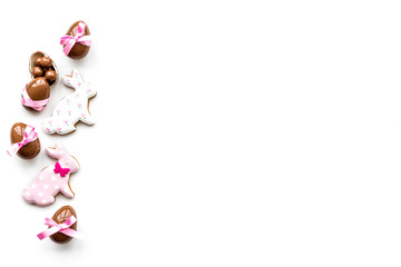 Sweets for Easter table. Chocolate eggs near cookies in shape of Easter bunny on white background top view copy space