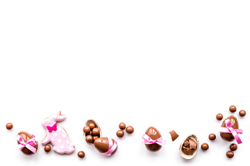 Sweets for Easter table. Chocolate eggs near cookies in shape of Easter bunny on white background top view copy space