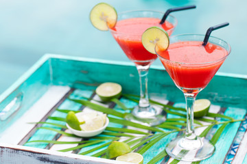 Strawberry margarita cocktail on colorful wooden background with palm leaf. Copy space