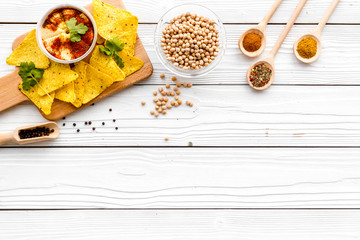 Serve hummus. Bowl with dish near pieces of crispbread on white wooden background top view copy space