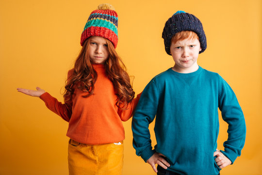Two confused little redhead children wearing warm hats.