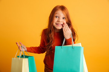 Happy little redhead girl holding shopping bags. Looking camera.