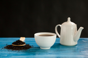 Obraz na płótnie Canvas Hot tea next to a spoon with tea leaves on vintage blue board over black background