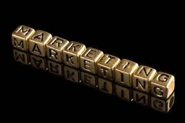 Gold alphabet block Lay stack the word "MARKETING" on black background.