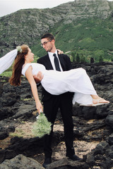 the groom is taking his bride in his arms. The bride 's neck is flying in the wind. Hawaii is also a mountain
