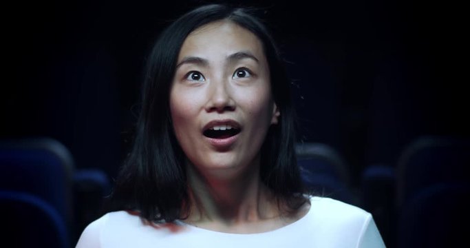 Close up, slow motion reaction shot of a Chinese girl reacting in awe in the movie theatre.