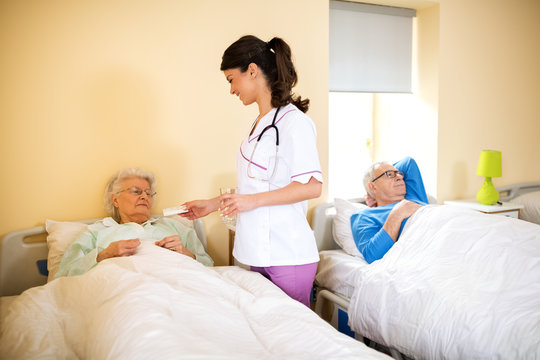 Nurse at nursing home brings medicine to senior immobile woman